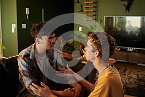 Young gay couple wearing casual clothing face to face while arguing in living room at home