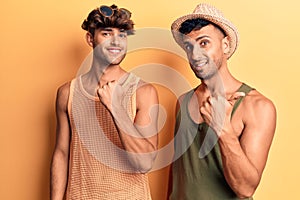 Young gay couple wearing summer clothes smiling with happy face looking and pointing to the side with thumb up