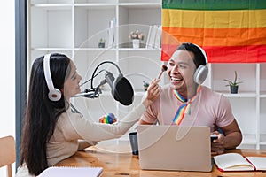 A young gay man and his girlfriend use a laptop and microphone to stream podcast audio at a studio talking about gender