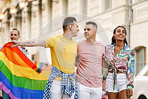 Young gay people holding rainbow flag during pride parade on street