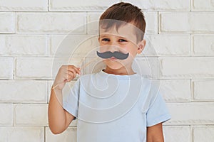 Young gentleman holding paper moustache with rather shrewd look