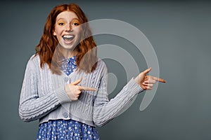 Young ginger excited woman exclaiming and pointing fingers aside
