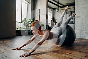 Young ginger sportive woman doing stretching exercises on stability exercise ball
