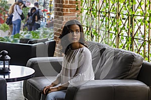 young girl from 19 to 25 years old sitting on black sofa in restaurant looking out the window