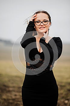 Young girl 20-25 years old in glasses and a black dress posing on a field background