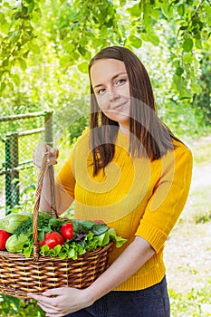 A young girl of 20-25 years old holds a basket with a crop against the background of a garden