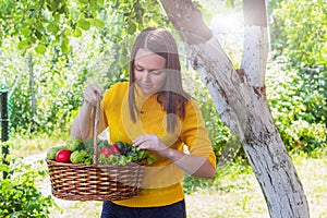 A young girl of 20-25 years old holds a basket with a crop against the background of a garden