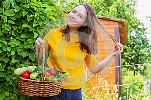 A young girl of 20-25 years old holds a basket with a crop against the background of a garden