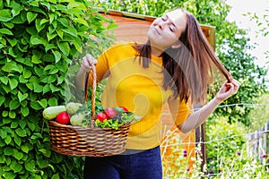 A young girl of 20-25 years old holds a basket with a crop against the background of a garden