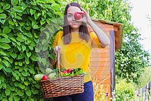 A young girl of 20-25 years old holds a basket with a crop against the background of a garden