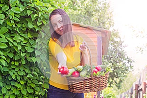 A young girl of 20-25 years old holds a basket with a crop against the background of a garden