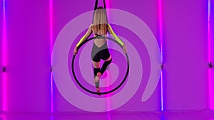 Young girl acrobat rotates in an air hoop and performs tricks while walking through the air. A circus performer in black