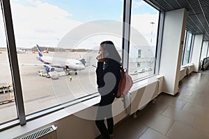 A young girl at the airport is talking on the phone.