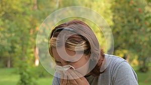 A young girl with allergies in an autumn park. Sneezing girl blows her nose into a napkin and sneezes. selective focus