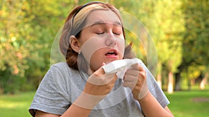 A young girl with allergies in an autumn park. Sneezing girl blows her nose into a napkin and sneezes. selective focus