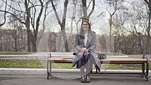 A young girl alone in a park on a bench sits and laughs. A young woman is sitting with a coffee on a bench in a park.