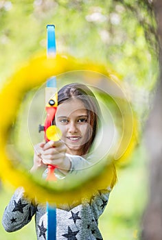 Young girl archer with bow aiming through flower wreath