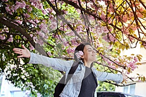 Young girl with arms wide open enjoying sunshine standing on the background of blooming sakura