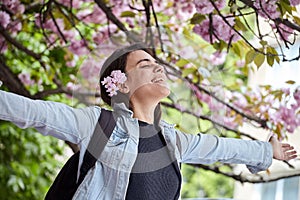 Young girl with arms wide open enjoying sunshine standing on the background of blooming sakura