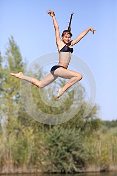 A young girl athlete in a bathing suit on the pier happily jumping into the water