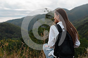 Young girl with a backpack against the background of mountains.