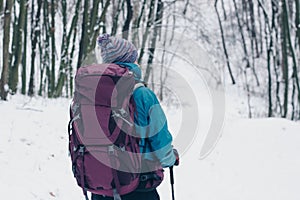 Young girl with backpack hiking downhill through the winter forest. Look from the back