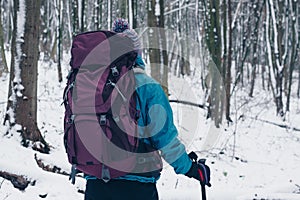 Young girl with backpack hiking through the winter forest. Look from the back