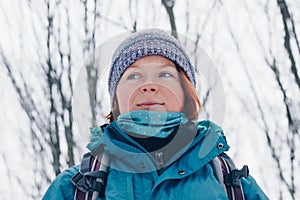 Young girl with backpack looks aside in the winter forest. View from below