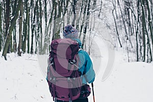 Young girl with backpack looks backward hiking through the winter forest