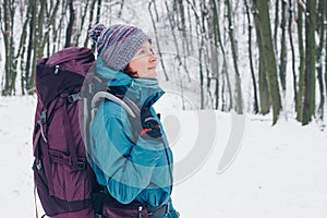 Young girl with backpack looks up hiking through the winter forest. Look from the right side