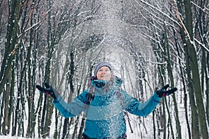 Young girl with backpack playing with snow in the winter forest