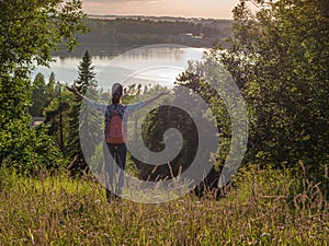 Young girl with a backpack, spreading hands with joy and inspiration facing the sun. Freedom concept