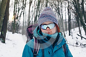 Young girl with backpack and sunglasses looks forward hiking through the winter forest