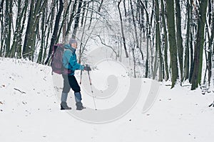 Young girl with backpack turns around while hiking on the path in the winter forest