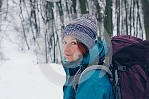 Young girl with backpack turns around while hiking through the winter forest