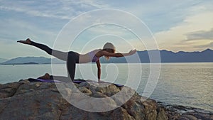 Young girl balances holding yoga pose against seascape