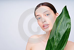 A young girl with bare shoulders holding a tropical leaf