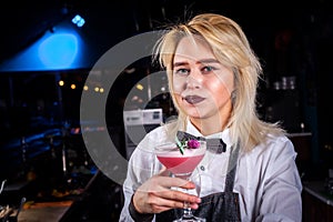 Young girl barman creates a cocktail while standing near the bar counter in pub