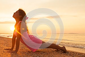 Young girl on beach at sunrise doing yoga exercise