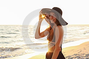 Young girl on the beach in a swimsuit, pareo, big straw hat