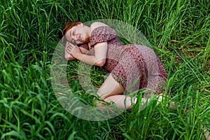 A young girl in a beautiful dress lies in the green grass