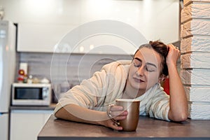 young girl with beautiful hair in a white coat drinking coffee in the kitchen in the morning.