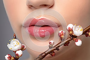 Young girl with beautiful nude make-up and plump lips. Perfect natural lips close up. Near her are beautiful blooming spring