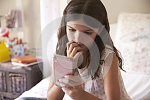 Young Girl In Bedroom Worried By Bullying Text Message