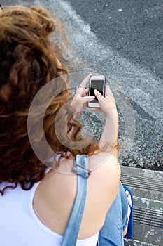 Young girl from behind holding cellphone and texting