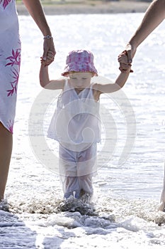 Young girl being walked on beach by parents