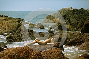 Young girl in bikini with beutiful body and sunglasses lying on the stones on the beach photo
