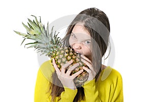 Young girl bites into a large ripe pineapple.