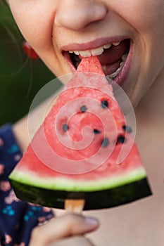 Young girl bites a slice of watermelon  snack on a stick - close up