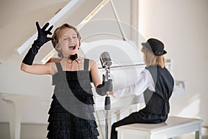 A young girl in a black dress singing into a microphone